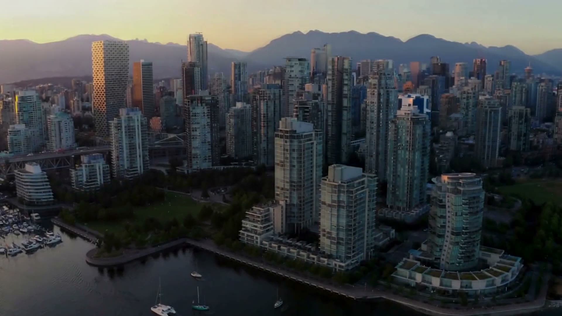 Aerial view of the Vancouver skyline at dusk, towers along the water with the North Shore mountains behind